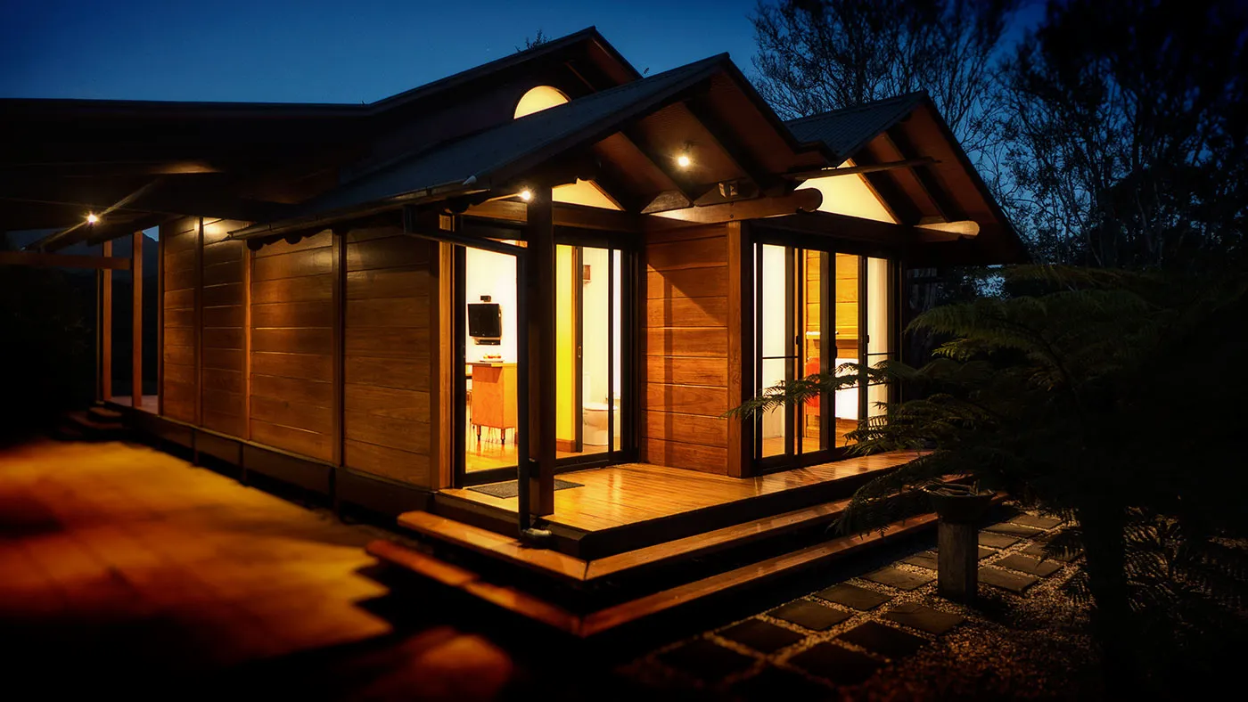 The Bower from behind at night — warm glow through windows against dark bush