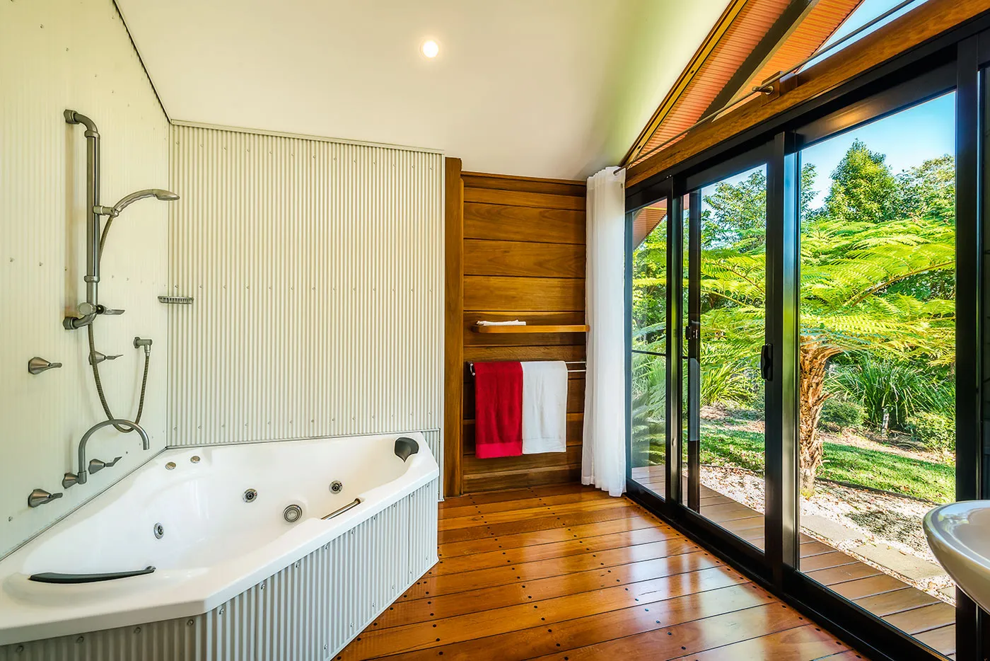 The Bower spa bath — sliding doors open onto a private garden with ferns and dappled light