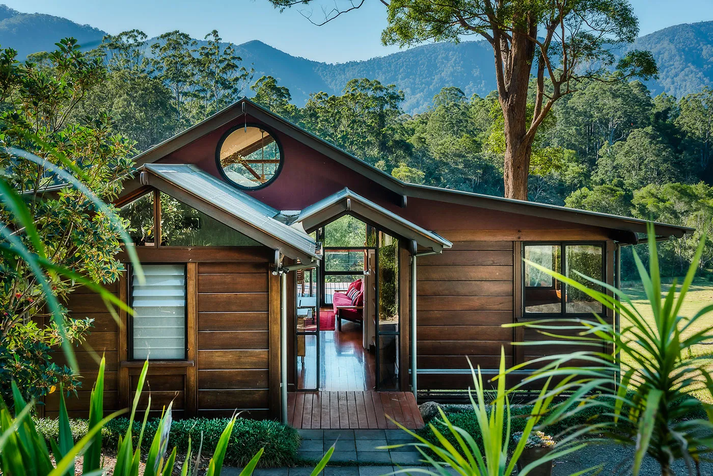 Tallowood chalet — timber exterior with a round window, the escarpment visible through the trees