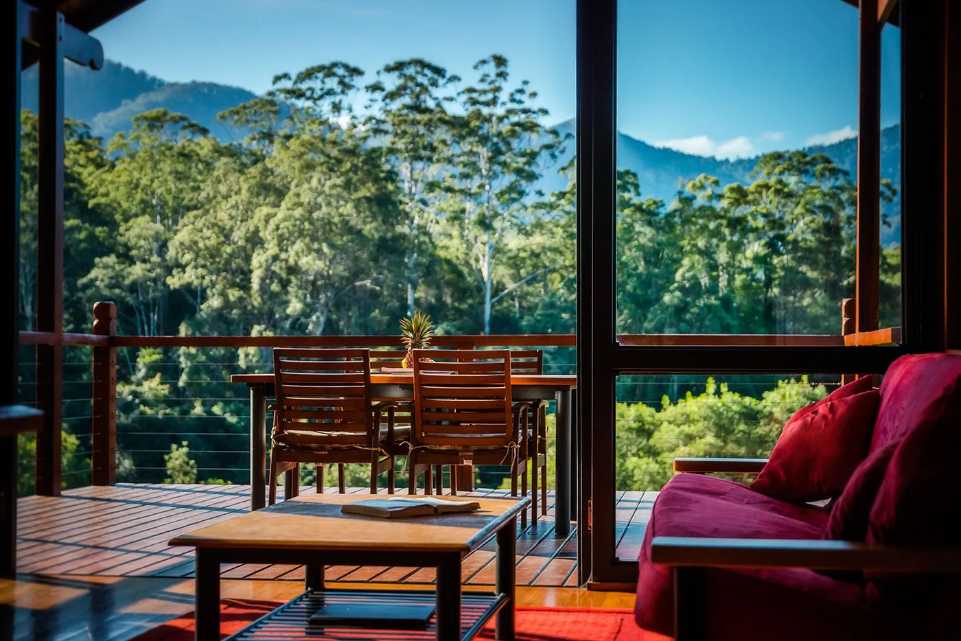 Living area opening onto a sun-drenched deck with views of forest canopy and distant mountains
